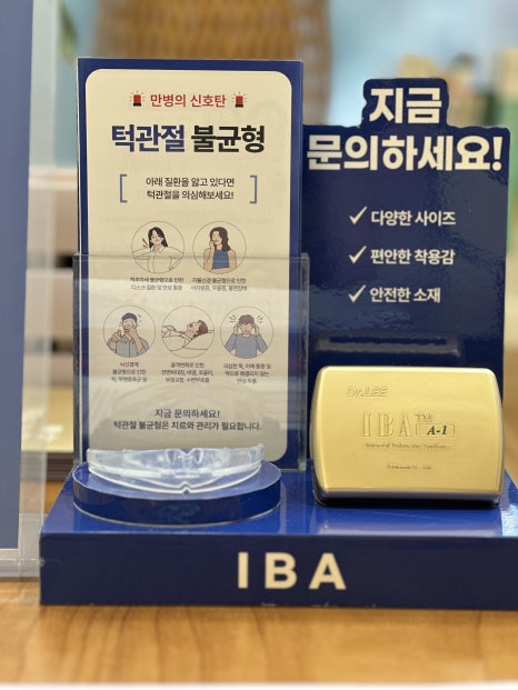 턱관절 불균형에 대한 정보가 담긴 안내판과 제품이 전시된 모습입니다. 안내판에는 다양한 증상과 해결 방법이 그림과 함께 설명되어 있으며, 옆에는 '지금 문의하세요!'라는 문구가 적혀 있습니다.